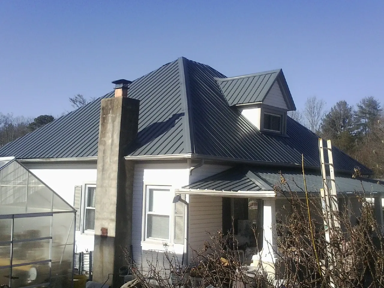 Dark blue standing seam metal roof on a white farmhouse with dormer — Slate & Tile Roof Repair by Roofing Brothers in Shannock