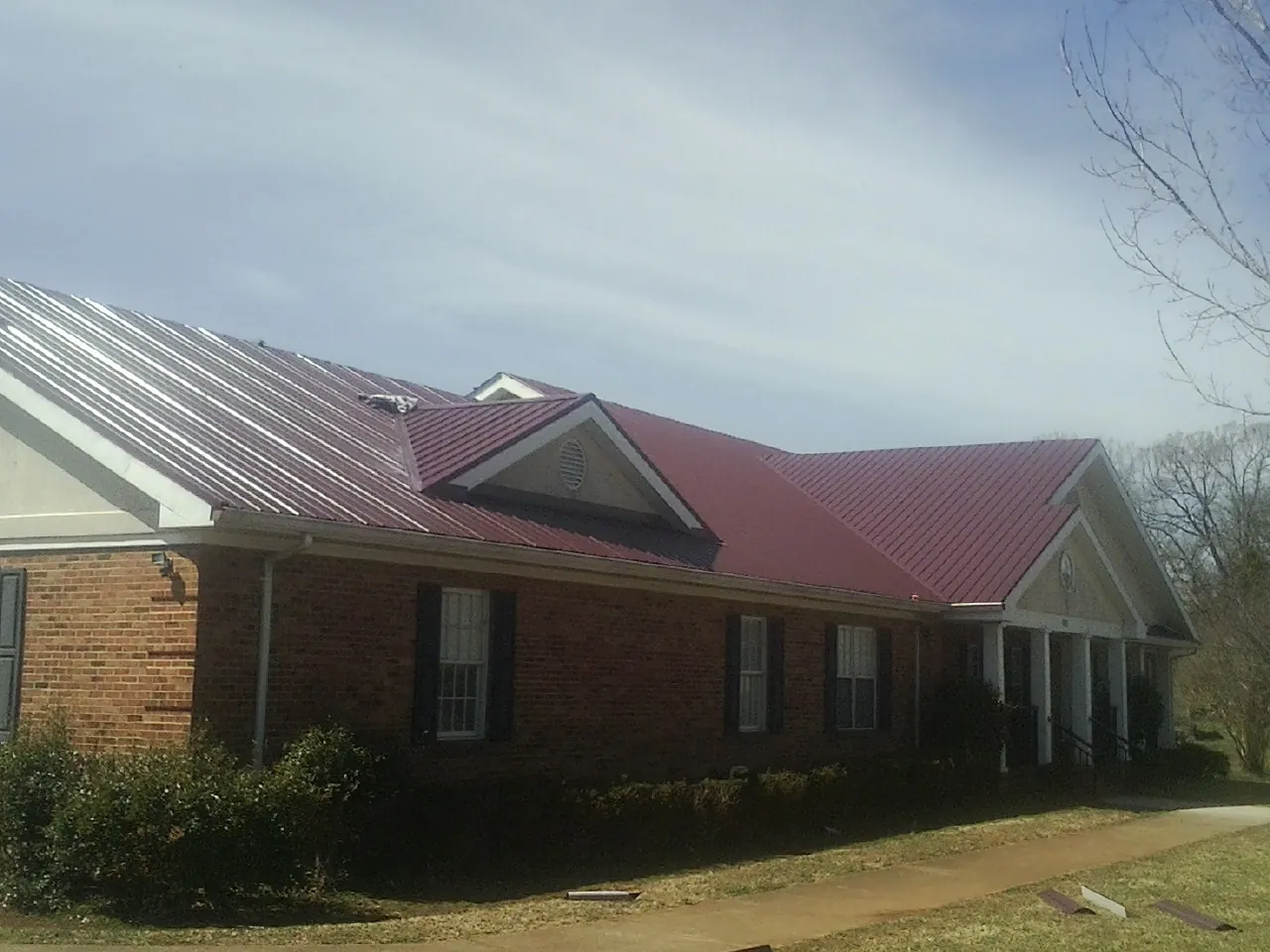Red metal roof with gabled entries on a long brick building, from a Hail Damage Roof Repair job in Shannock
