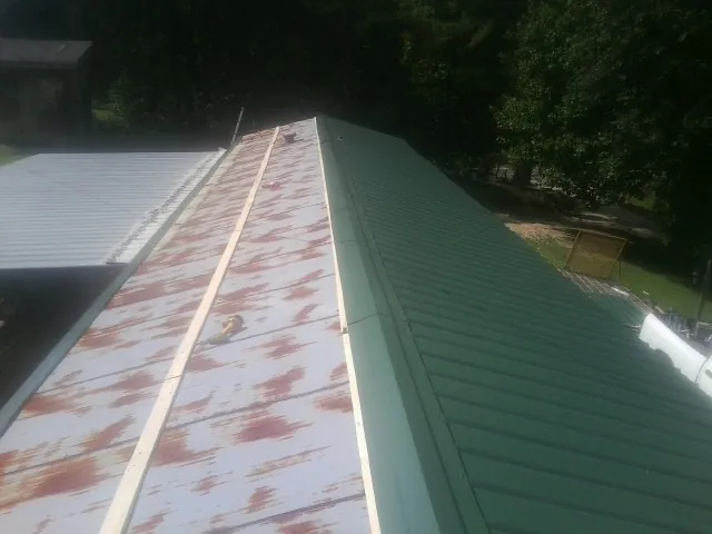 Old rusted panels beside newly installed green metal roofing — Wind Damage Roof Repair by Roofing Brothers in Shannock
