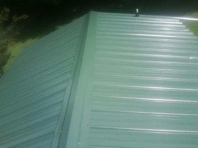 New green metal panels meeting at the ridge of a roof — Flat Roof Repair work by our crew in Shannock