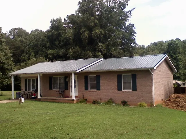 Gray metal roof on a brick ranch house with a side carport in Shannock