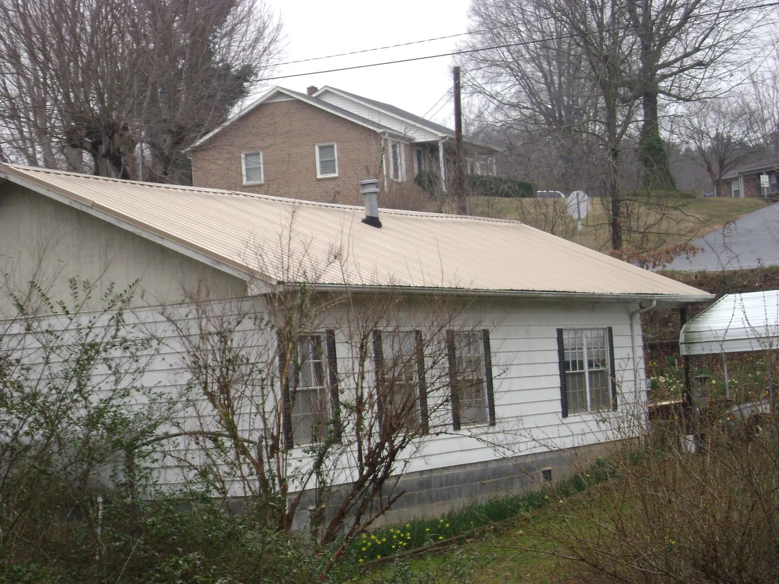 Tan metal roof on a white sided house set into a hillside — Commercial Roofing by Roofing Brothers in Shannock