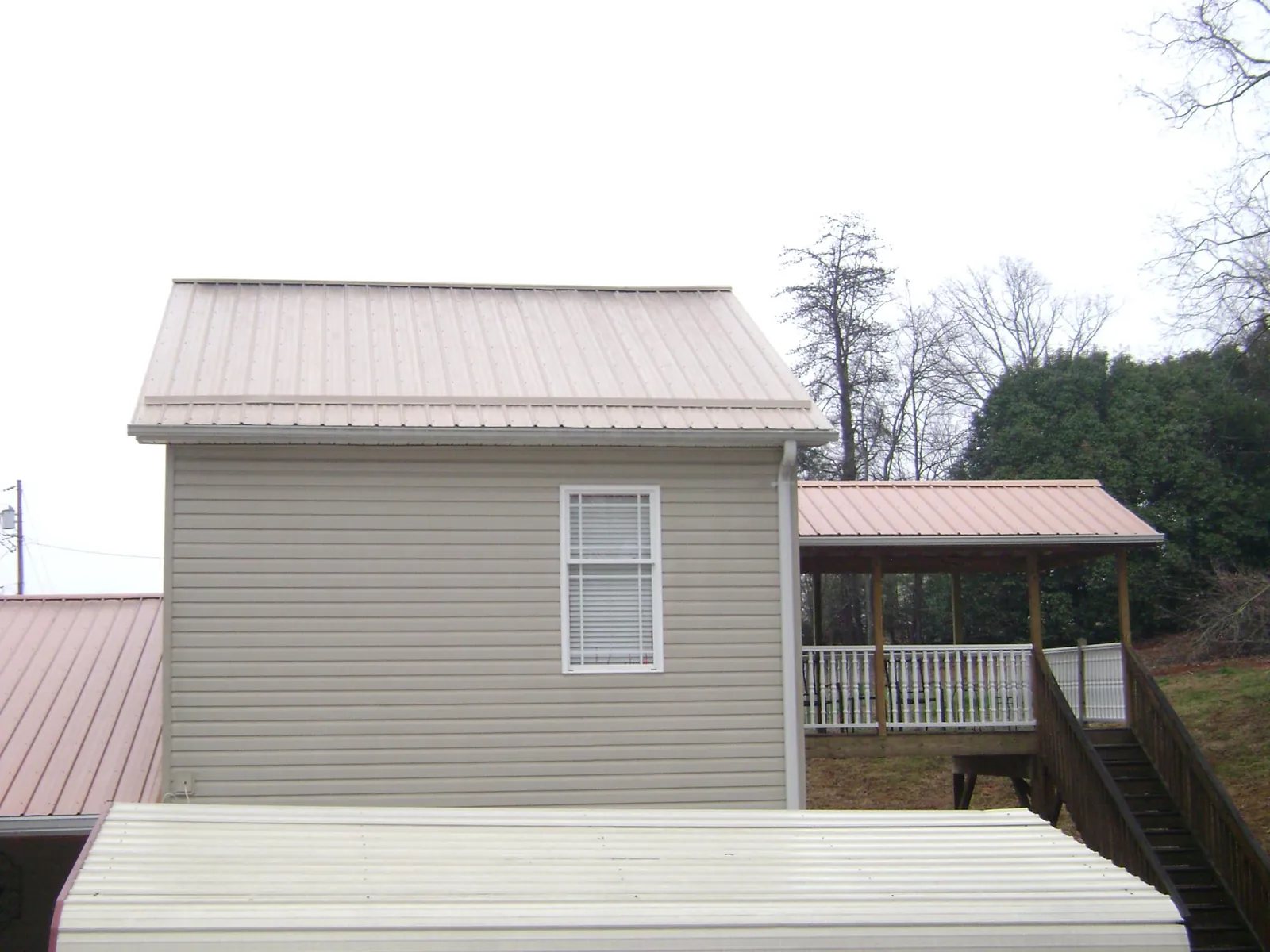 Tan metal roofs on a two story addition and attached porch, from a Roof Replacement job in Shannock